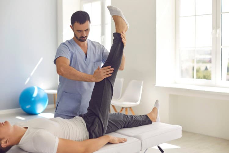 Physiotherapist stretching athletes leg for injury recovery session - One Body LDN Physiotherapist stretching athlete's leg for injury recovery session