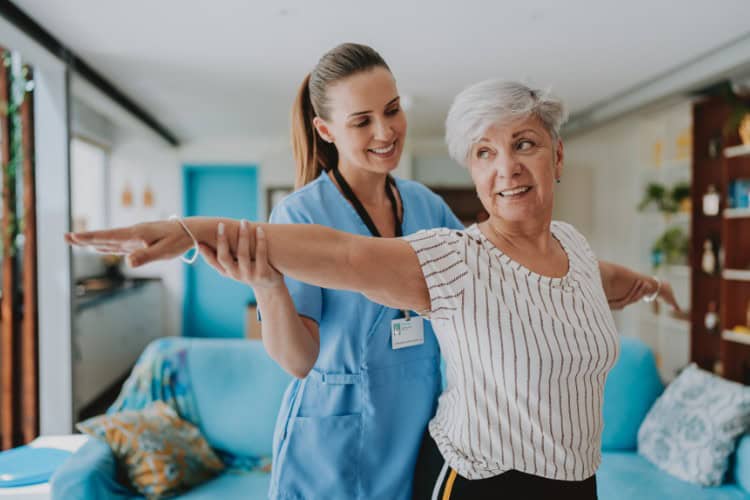 Smiling senior woman doing balance exercise with physiotherapist - One Body LDN Smiling senior woman doing balance exercise with physiotherapist