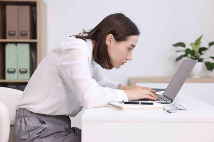 Woman with poor posture at desk needing physiotherapy support - One Body LDN Woman with poor posture at desk needing physiotherapy support