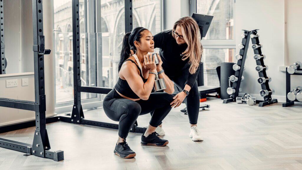 Trainer coaching woman during weighted squat exercise in gym