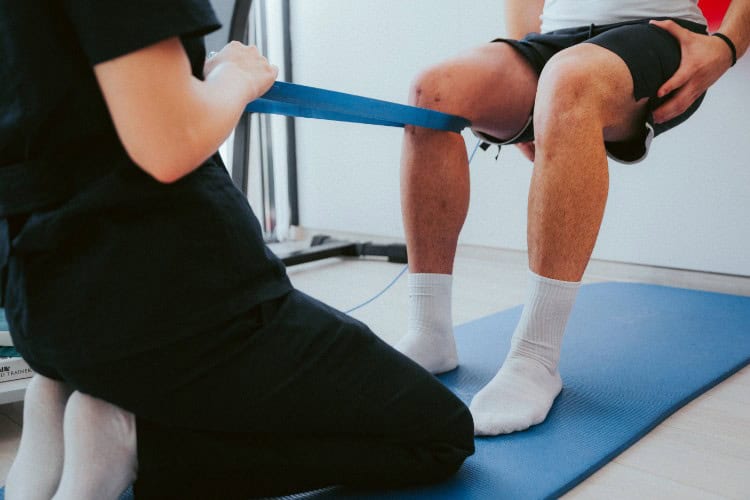 Sports physiotherapist guiding knee resistance exercise during rehab session