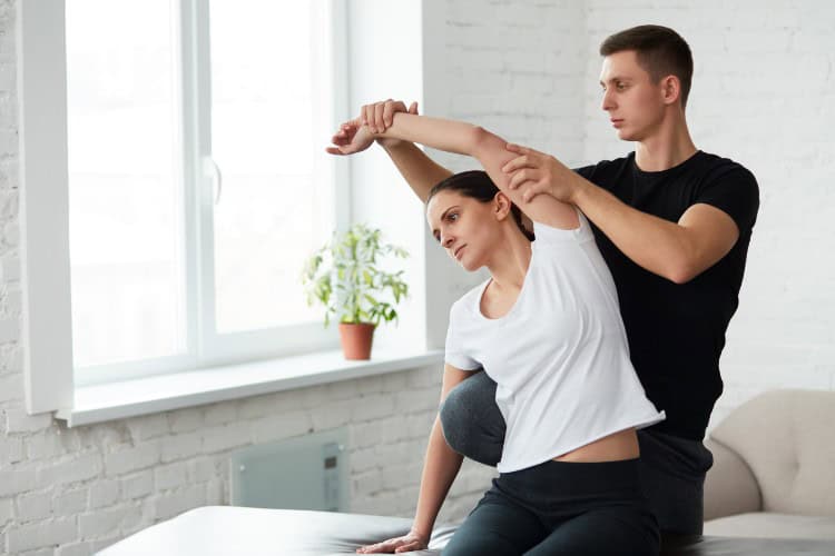 Therapist assisting woman with shoulder stretch after massage session