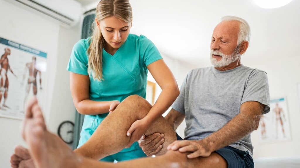 Therapist treating elderly patient with severe knee pain Physiotherapy in London