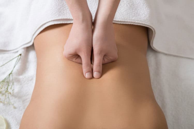 Therapist using thumb pressure for lower back massage - One Body LDN Therapist using thumb pressure for lower back massage