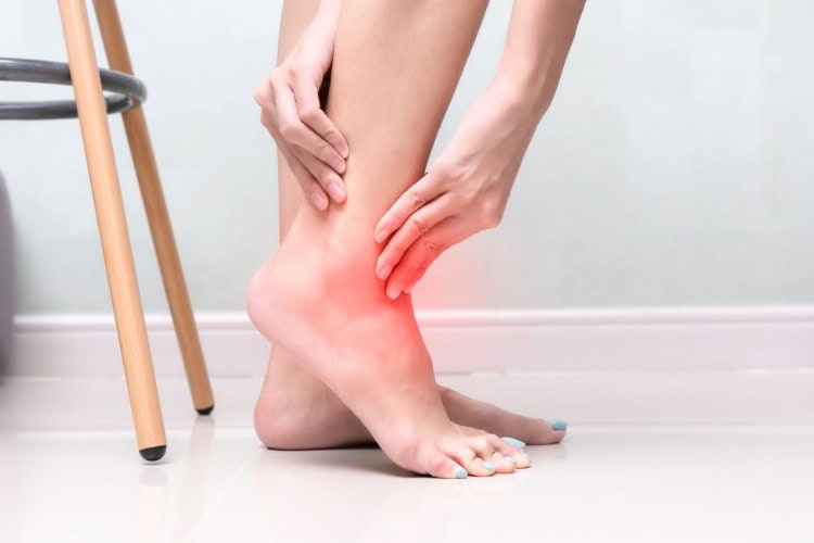 Woman holding swollen ankle with visible pain and inflammation - One Body LDN Woman holding swollen ankle with visible pain and inflammation