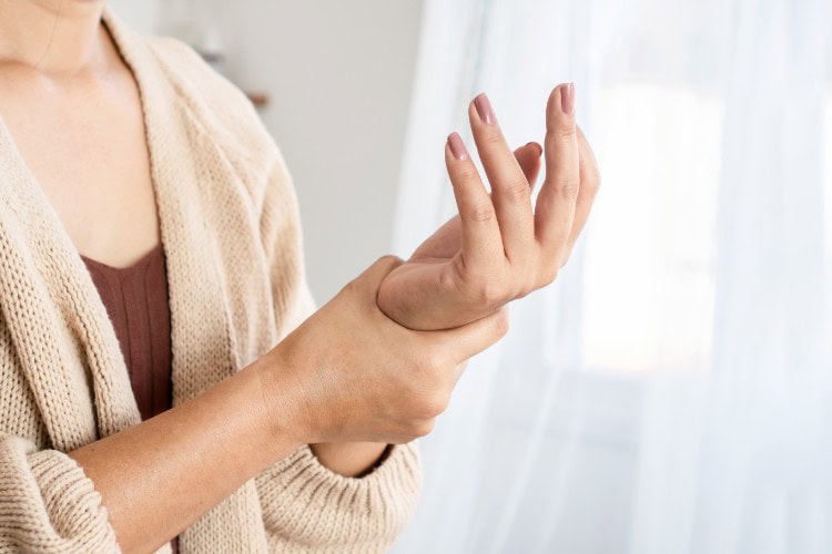 Woman holding wrist in pain showing early signs of hand strain - One Body LDN Woman holding wrist in pain showing early signs of hand strain
