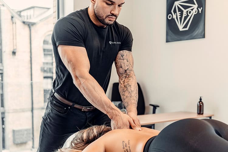 Physiotherapist performing a sports massage on a client’s back at One Body clinic