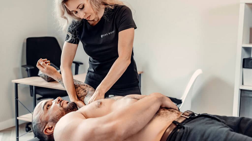 Sports therapist applying deep tissue massage to an athlete’s shoulder at One Body clinic