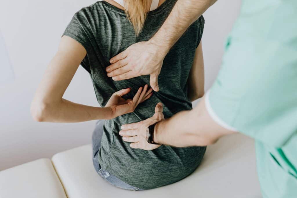 Physiotherapist examining a patient's lower back for pain assessment in clinic.